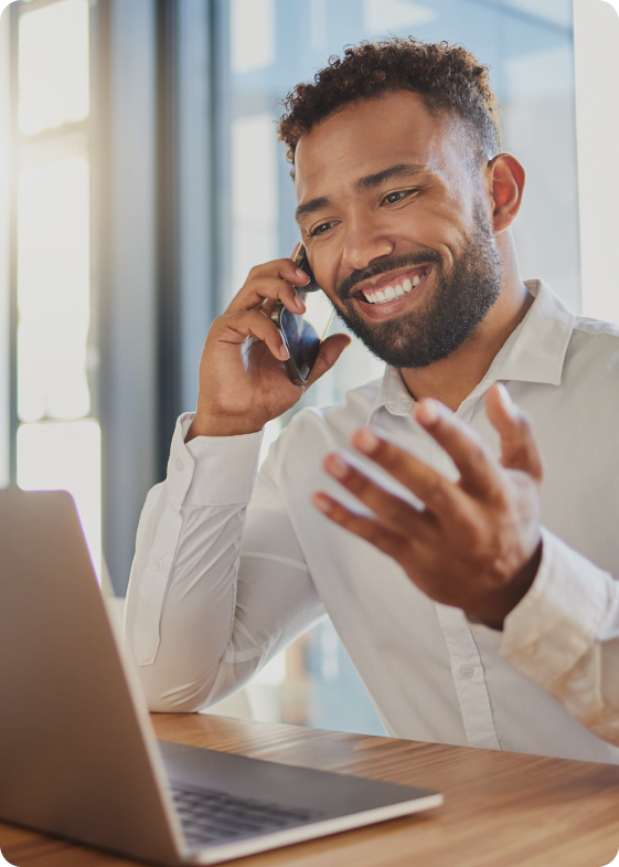 Homem alegre conversando ao telefone e usando um computador, refletindo a eficácia da comunicação na transformação digital.